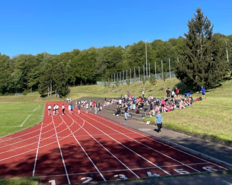 Schüler*innen stehen auf der Laufbahn und sitzen auf der Zuschauertreppe