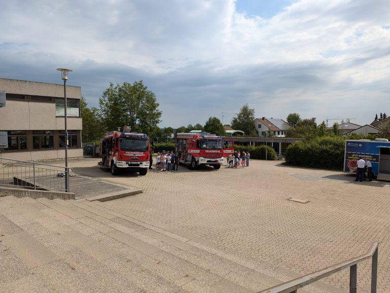 Zwei Feuerwehrfahrzeuge werden auf dem Schulhof präsentiert